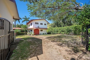 A two-story house with a red door, surrounded by a well-maintained lawn and various trees. - Santa Cruz Group Getaway w/ Pool: Walk to Beach (Junquillal)
