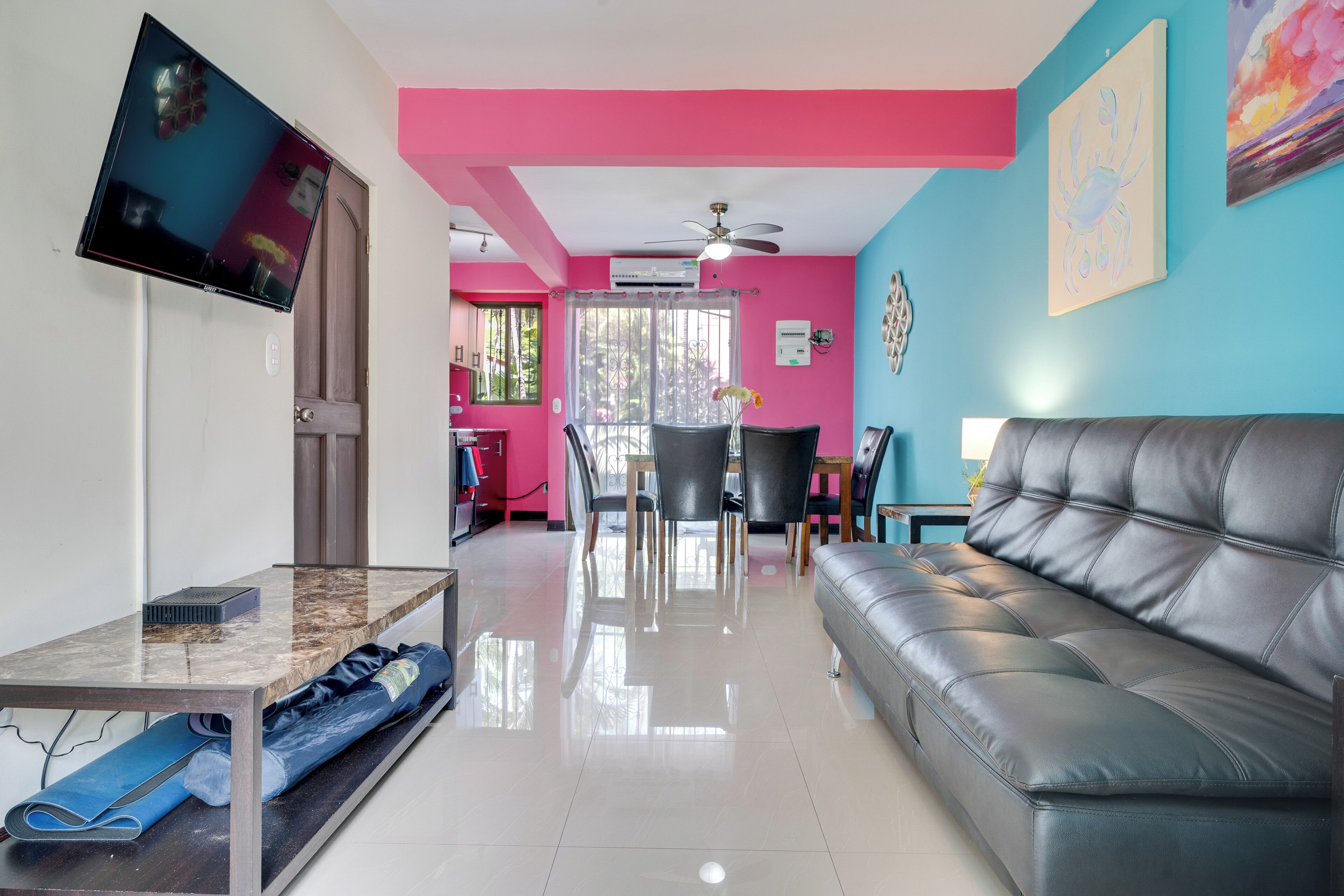 A modern living room with a leather sofa, a flat-screen TV, a dining area with chairs, and a kitchen in the background.