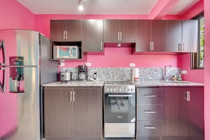 A modern kitchen with stainless steel appliances, wooden cabinets, and a pink wall. - Playas del Coco: Pool & Private Terrace (Playas del Coco)