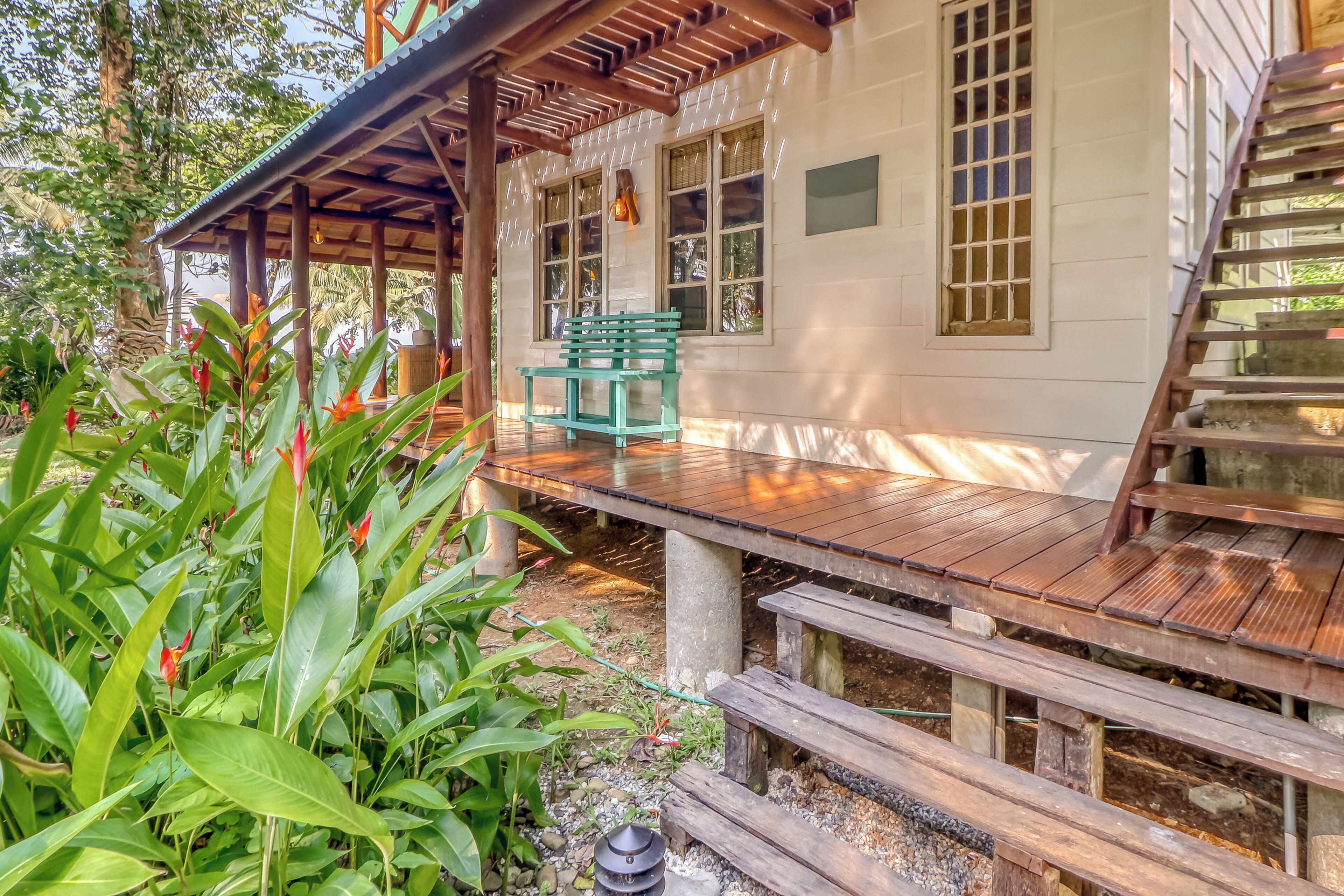 A wooden deck with a bench, a covered area with a pergola, and a house with windows.