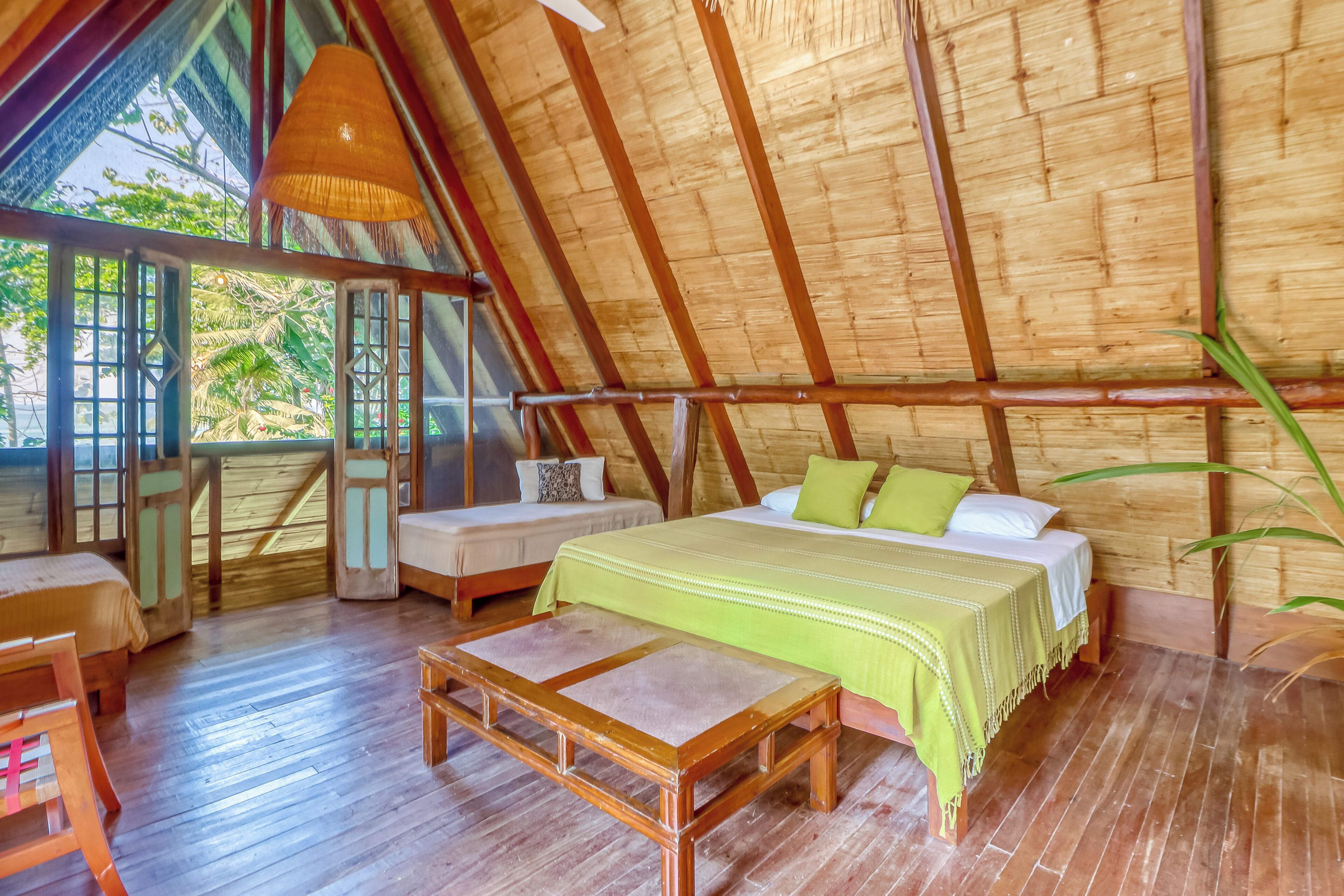 A room with a sloped ceiling, wooden flooring, a bed with pillows, a bench, and a table.