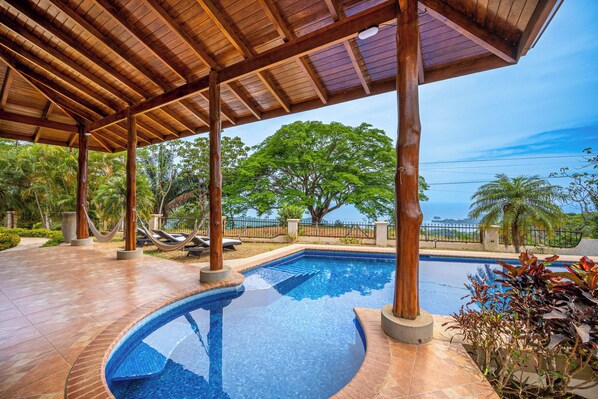 A pool area with a wooden pergola, lounge chairs, and a view of the ocean. - Luxe Ocean-View Hideaway in Carrillo (Playa Carrillo)