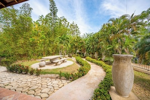 Un jardí amb un camí de pedra, una zona central amb bancs i una gran jardiniera de pedra.