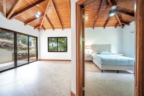 A bedroom with a bed, a nightstand, and a window with a view of greenery. - Luxe Ocean-View Hideaway in Carrillo (Playa Carrillo)