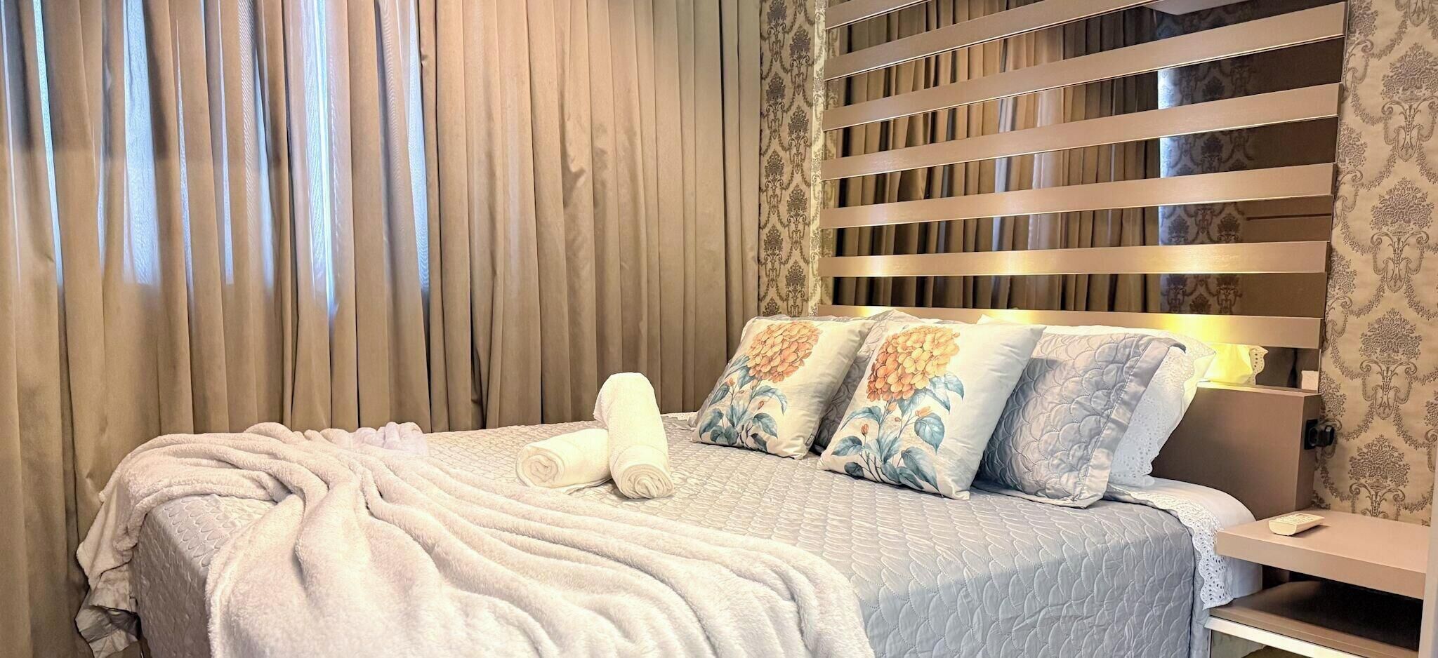 A hotel room with a bed, a nightstand, and a window with curtains.