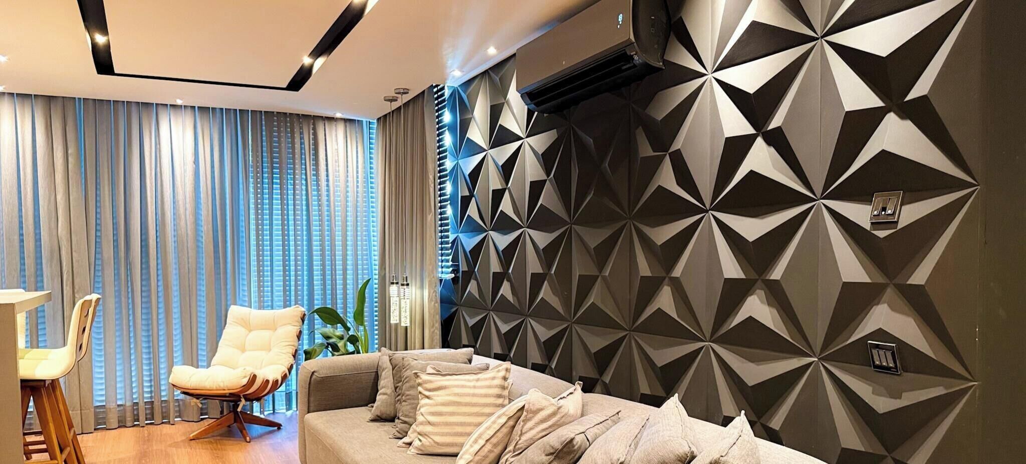 Uma sala de estar moderna com uma parede estampada em padrão geométrico, um sofá, uma poltrona e um espaço de jantar com mesa e cadeiras.