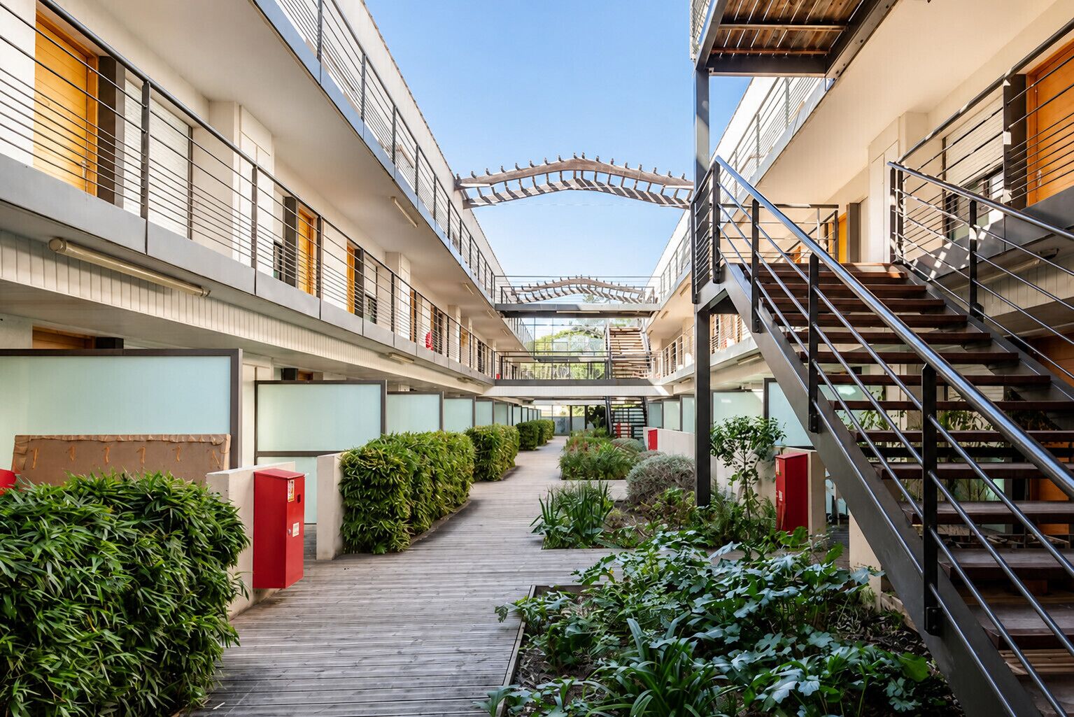 Un couloir d’hôtel à plusieurs niveaux, avec une allée centrale, des escaliers de part et d’autre, et un espace extérieur abrité.