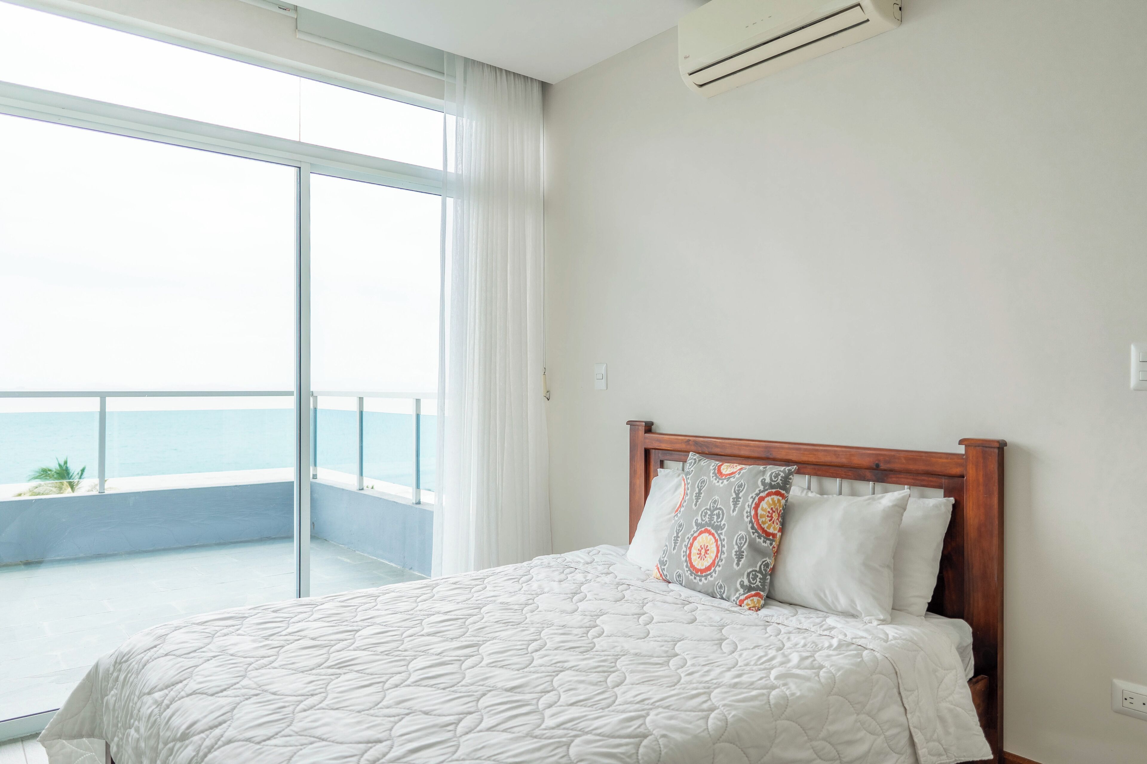 A bedroom with a bed, a window with a view of the sea, and an air conditioning unit.