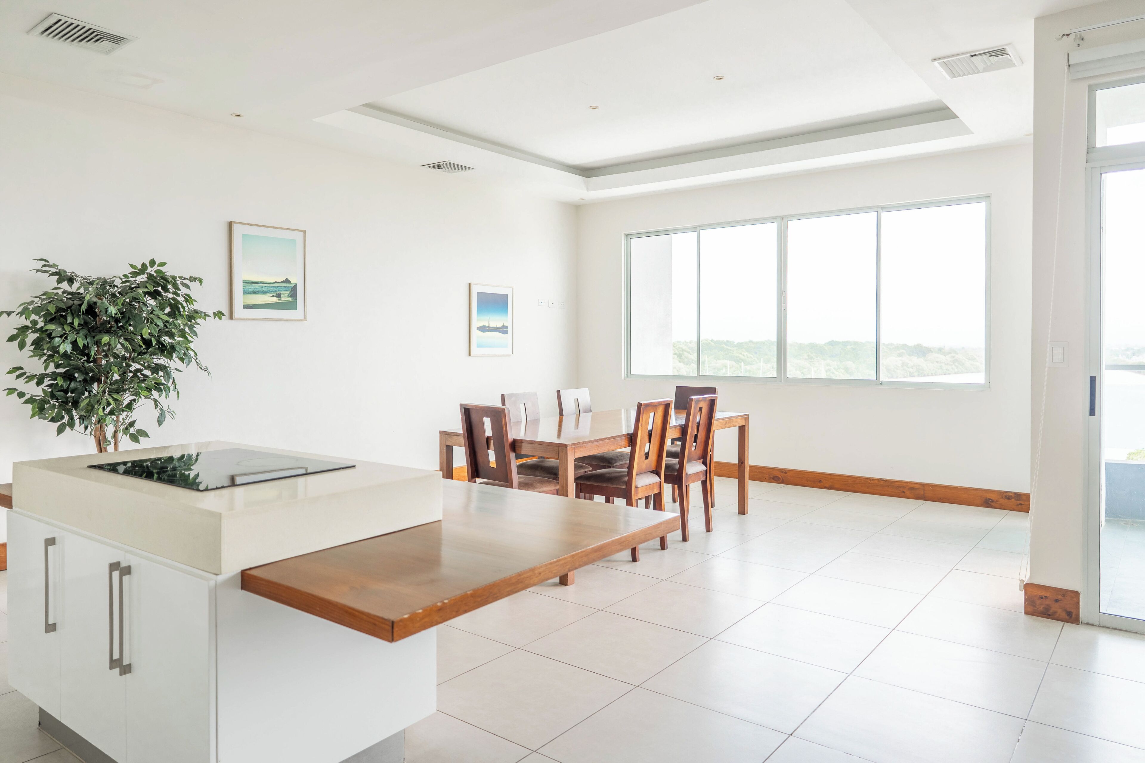 A modern kitchen with a dining area, large windows, and a view of the outdoors.