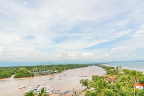 A coastal area with boats docked along the shore, a bridge connecting the land to the water, and a beach with a road running parallel to the coast. - El Roble Penthouse: Wraparound Deck, Views (El Roble)