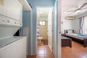 Ein kompaktes Hotelzimmer mit Küchenzeile, einem Bett, einem kleinen Tisch und einem durch eine offene Tür einsehbaren Badezimmer.