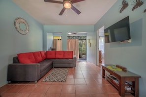 A living room with a sectional sofa, a flat-screen TV, a ceiling fan, and a view to the outside. - Walk to Playa Ocotal! 2BR Condo w/ Pool (Playa Ocotal)