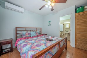 A bedroom with a wooden bed, a nightstand, a ceiling fan, and a bathroom visible through an open door. - Walk to Playa Ocotal! 2BR Condo w/ Pool (Playa Ocotal)