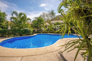 Ein Pool mit geschwungener Kante, umgeben von Palmen und anderer Vegetation.