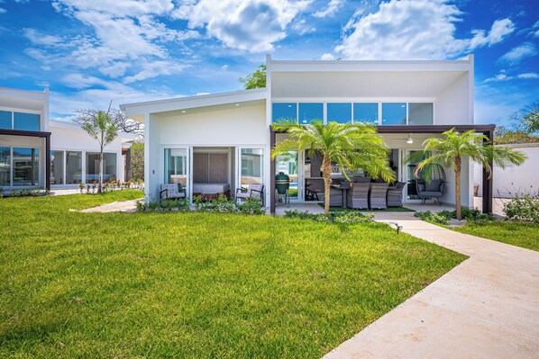 A modern two-story house with a well-maintained lawn, outdoor seating area, and a view of the sky. - Playa Avellanas Villa: Modern Luxury, Pool, Views (Playa Avellanas)