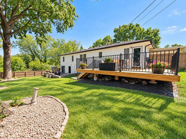 A two-story house with a deck, outdoor seating, and a stone foundation.
