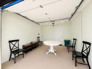 Une pièce avec une table blanche, quatre chaises noires, un banc et une porte blanche.