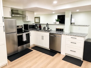 A modern kitchen with stainless steel appliances, white cabinetry, and a granite countertop.