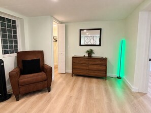A room with a brown leather chair, a wooden dresser, and a green light strip.