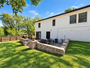 Une maison blanche avec un patio en pierre, un barbecue et une table avec des chaises.