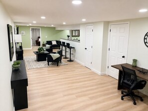 A modern living room with a sofa, coffee table, and chairs, a kitchen area with a countertop and cabinets, and a dining area with a table and chairs.