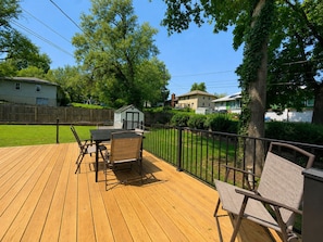 A wooden deck with outdoor furniture, a small shed, and a fenced yard with houses in the background. - The KC Garden Retreat- 10 Mins to Everything! (Kansas City)