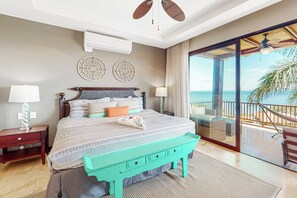 A bedroom with a bed, bedside tables, a bench, a view of the sea, and a ceiling fan. - Ocotal Hilltop Condo: Ocean Views, Pool Access (Playa Ocotal)