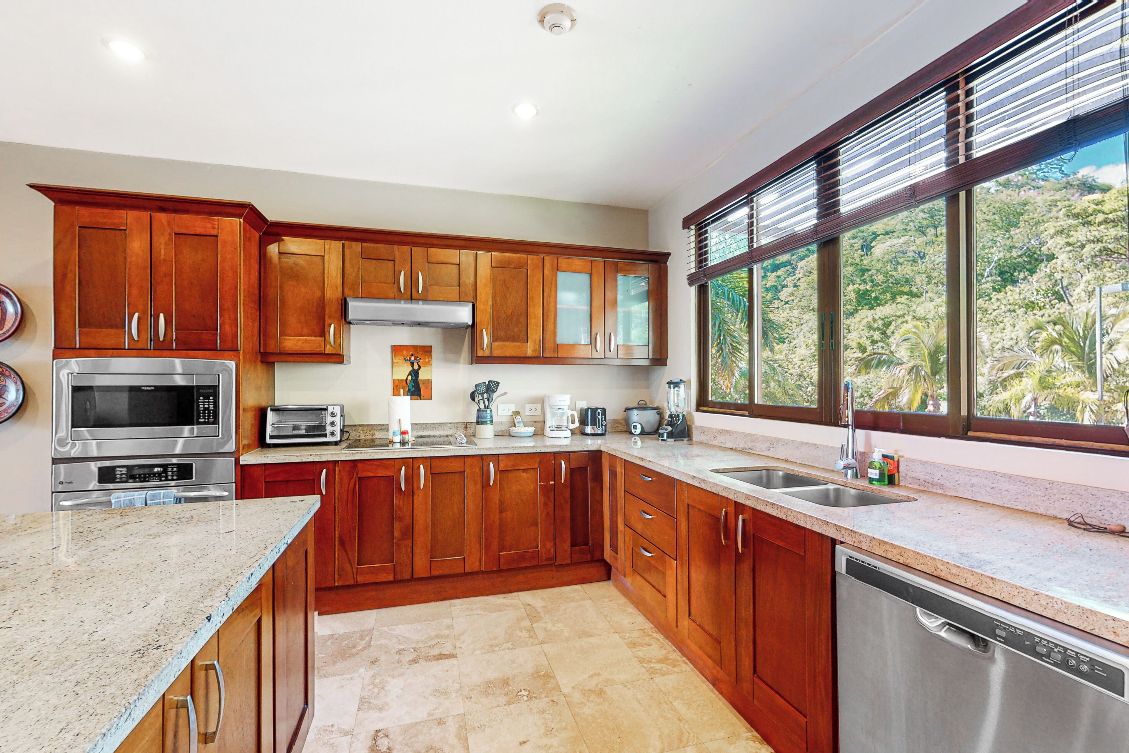 Une cuisine moderne avec des meubles en bois, des appareils électroménagers en acier inoxydable et une grande fenêtre donnant sur un paysage verdoyant.