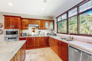 A modern kitchen with wooden cabinets, stainless steel appliances, and a large window offering a view of greenery.