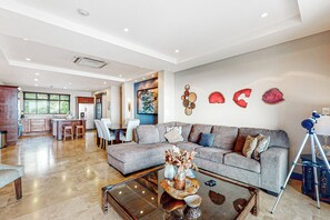 A spacious living area with a grey sofa, a coffee table with decorative items, and a wall with abstract art.