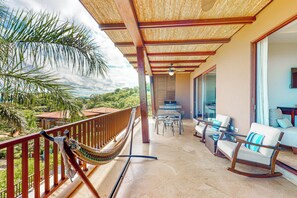 A balcony with a hammock, outdoor seating, and a view of the landscape. - Ocotal Hilltop Condo: Ocean Views, Pool Access (Playa Ocotal)