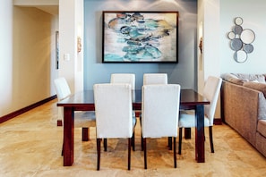 A dining area with a rectangular table and four chairs, a blue wall, and a decorative painting above the table.