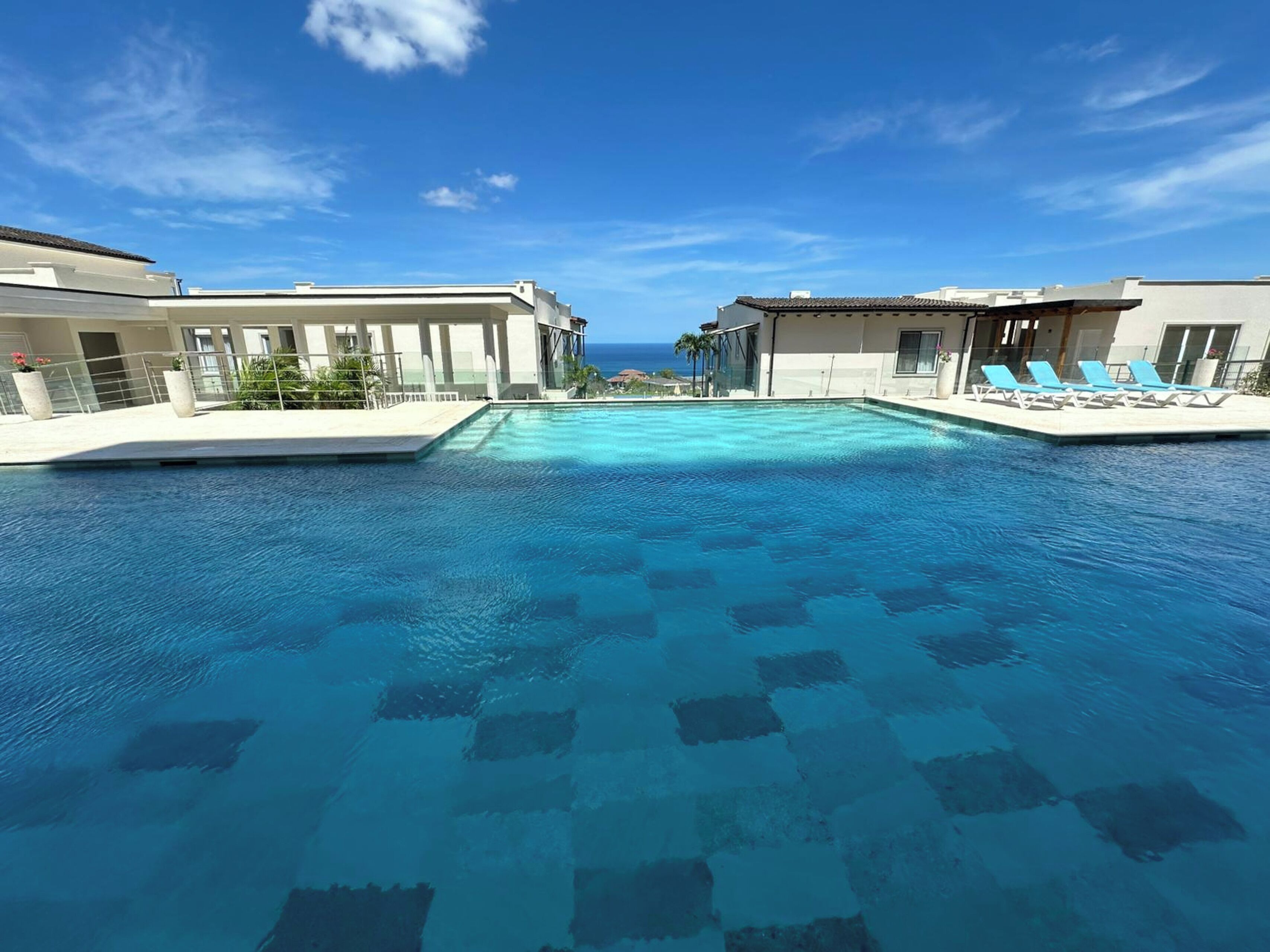 Uma piscina com água azul cristalina, rodeada por edifícios com varandas e espreguiçadeiras.