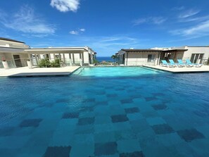 A swimming pool with clear blue water, surrounded by buildings with balconies and lounge chairs. - Ocean-View Tamarindo: Community Pool Access (Tamarindo)