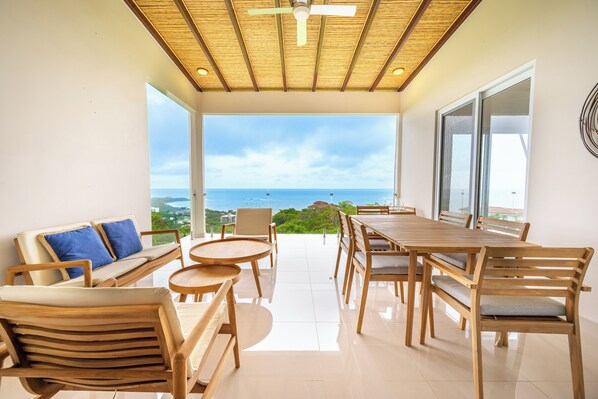 A spacious balcony with a wooden table and chairs, a sofa with cushions, and a view of the sea. - Ocean-View Tamarindo: Community Pool Access (Tamarindo)
