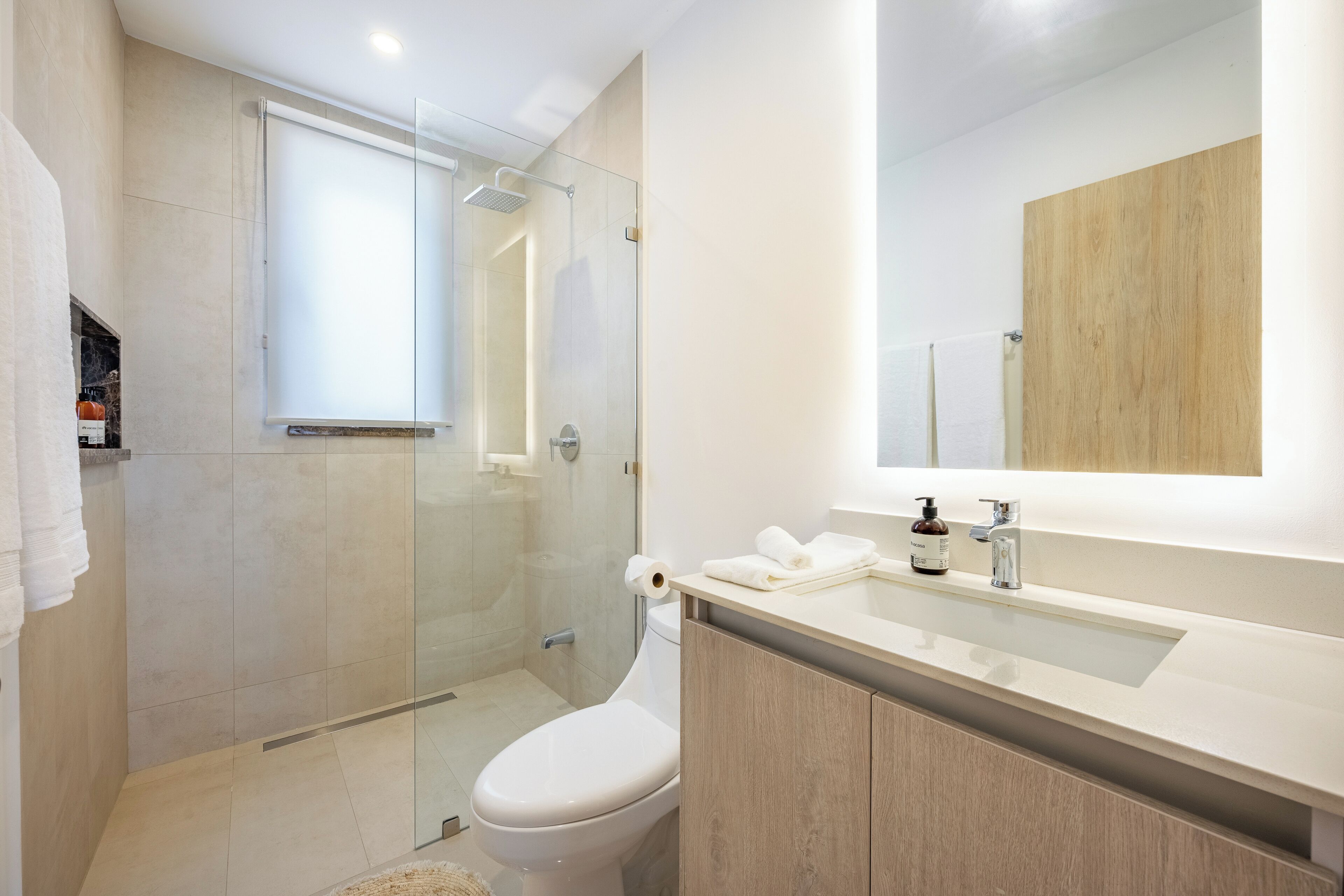 Une salle de bain moderne avec une douche à parois de verre, des toilettes, un lavabo avec un miroir et un meuble en bois.