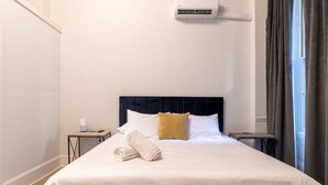 Habitació d'hotel amb un llit, una taula de nit, cortines a la finestra i un aparell d'aire condicionat.