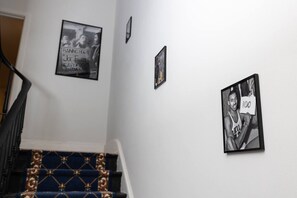 Eine Treppe mit blauem, gemustertem Teppich und Geländer, die zu einer Empore mit drei gerahmten Fotografien an der Wand führt.