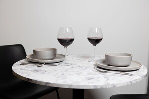 Een ronde marmeren tafel met twee witte kommen, twee wijnglazen en bestek.