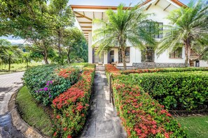A house with a paved pathway leading to the entrance, surrounded by lush greenery and flowering plants. - Private Pool, Luxe Patio: 4BR Carrillo Villa (Playas del Coco)