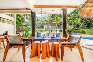 A modern outdoor seating area with wooden furniture and a pool. - Private Pool, Luxe Patio: 4BR Carrillo Villa (Playas del Coco)