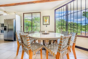 A dining area with a round table and chairs, a refrigerator, and a window with a view of greenery.