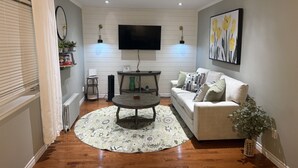A living room with a sofa, coffee table, and a flat-screen TV mounted on the wall. - Grand Falls-Windsor Gem | King Bed + Movie Room (Grand Falls-Windsor)