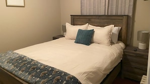 A neatly made bed with a patterned bedspread, a wooden headboard, and a bedside table with a lamp and a small decorative item.