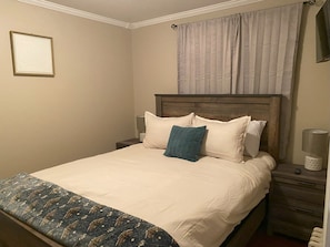 A neatly made bed with a patterned bedspread, a wooden headboard, and a bedside table with a lamp and a small decorative item.