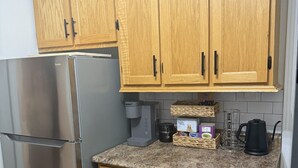 A kitchen with wooden cabinets, a stainless steel refrigerator, a coffee maker, and a kettle on the countertop.
