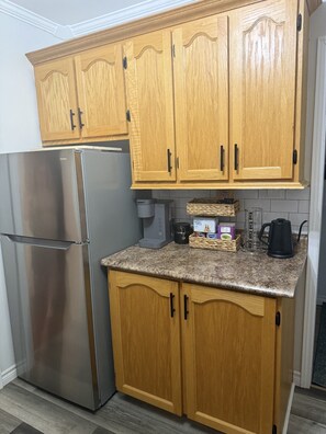 A kitchen with wooden cabinets, a stainless steel refrigerator, a coffee maker, and a kettle on the countertop.