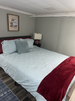 A bedroom with a bed, pillows, a nightstand, a lamp, and a framed picture on the wall.