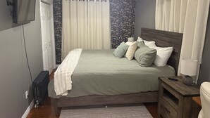A bedroom with a bed, bedside table, lamp, and a television on the wall. - Grand Falls-Windsor Gem | King Bed + Movie Room (Grand Falls-Windsor)