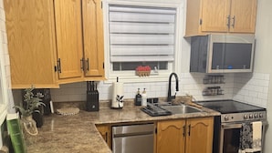 A compact kitchen with wooden cabinets, a stainless steel dishwasher, a stove, and a microwave.